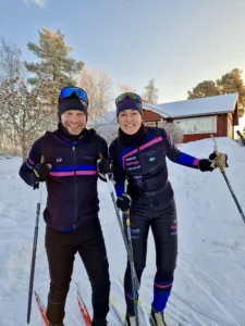 Två skidåkare i Västerås XC Ski kläder med Surahammars SOK-logotypen framför ett snötäckt landskap.